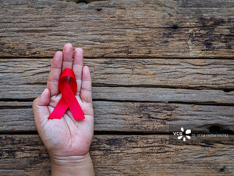 医疗保健理念——女性手握红色艾滋病意识丝带，木制背景。世界艾滋病日。图片素材