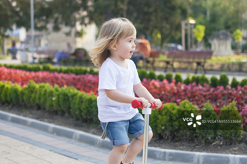一个金发小男孩在公园里骑滑板车图片素材