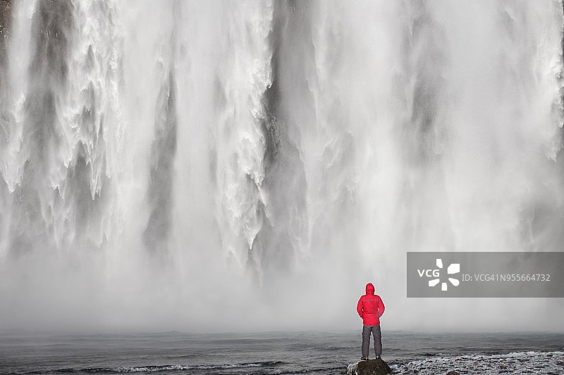 身穿红色夹克的旅游摄影师站在斯科加瀑布前，冰岛斯科加图片素材