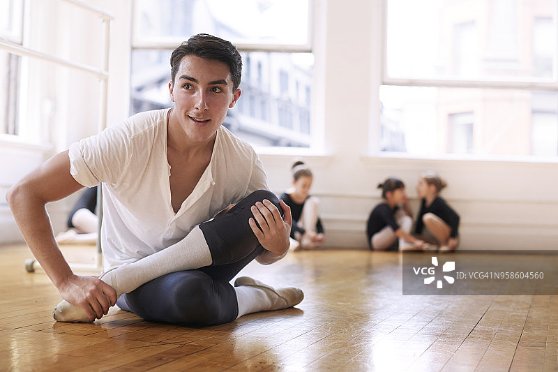 微笑的芭蕾舞者坐在工作室的硬木地板上锻炼图片素材
