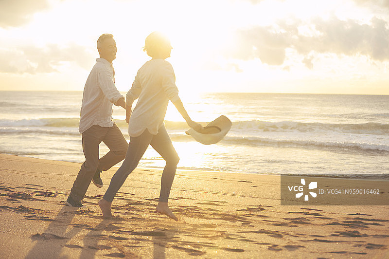 成熟的夫妇在日落或日出时在海滩上奔跑和玩耍。图片素材
