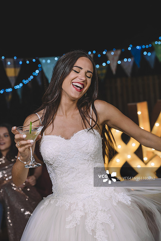快乐的新娘笑着跳舞，在一个户外晚会上拿着鸡尾酒图片素材