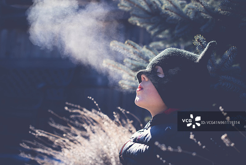 冬天在院子里吹气，闭着眼睛戴着针织帽的顽皮男孩图片素材