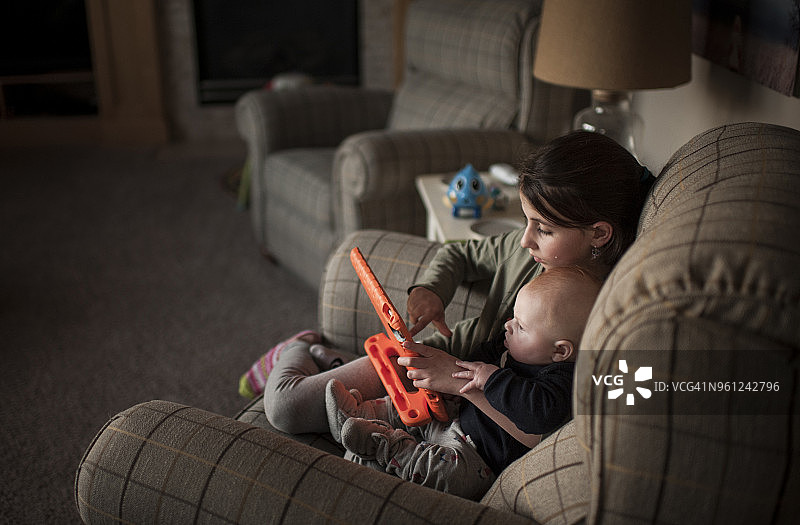 女孩拿着玩具，和哥哥在家里的扶手椅上玩图片素材