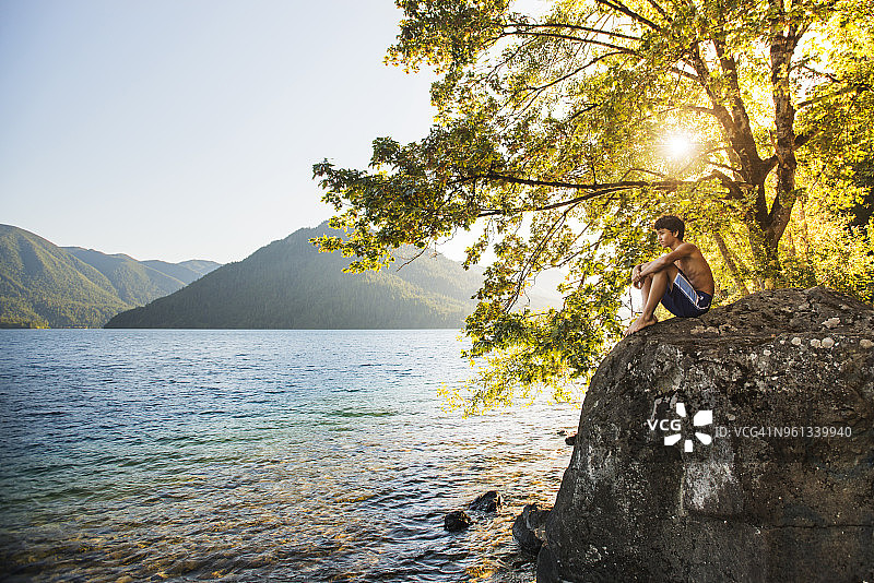 在阳光明媚的日子里，一个体贴的少年躺在岩石上看着湖面图片素材