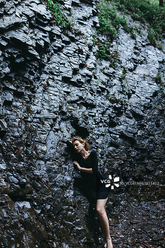 年轻女子靠着一块巨石站着图片素材
