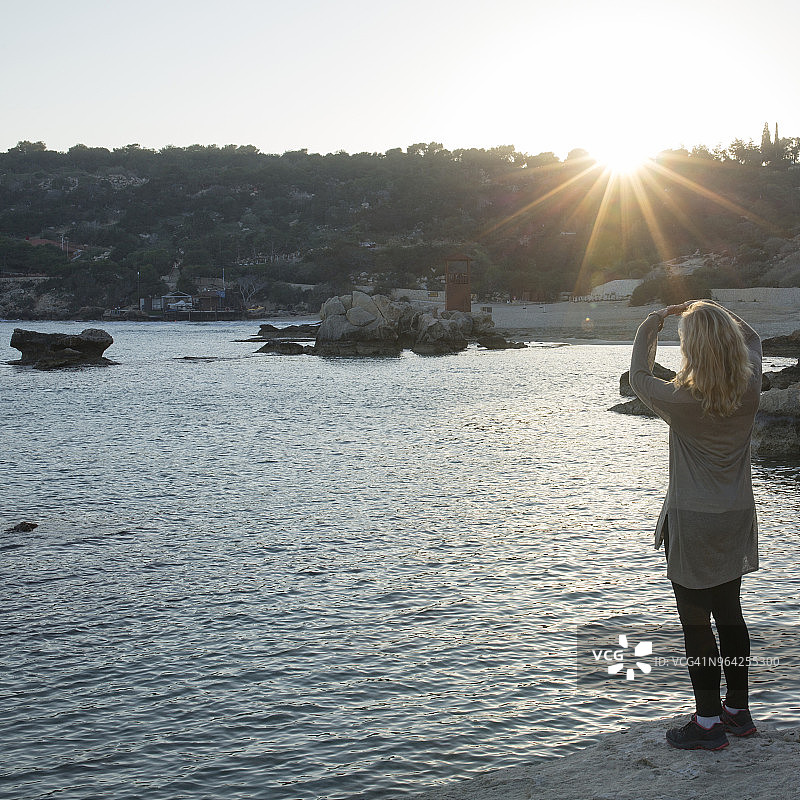 一个女人用手机在海港的日落上拍照图片素材