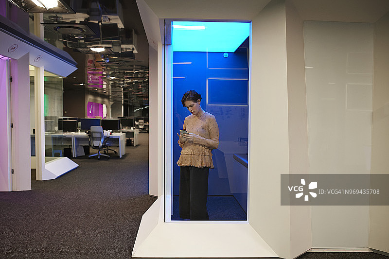 年轻女商人在公司办公室的“电话亭”里查看智能手机图片素材
