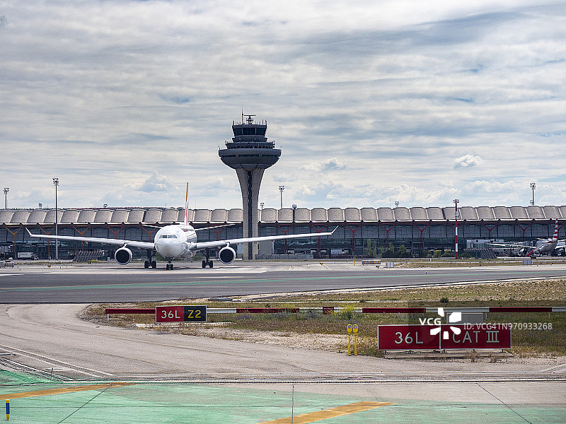 航站楼和机场塔台的控制与飞机在轨道上。马德里,西班牙。图片素材