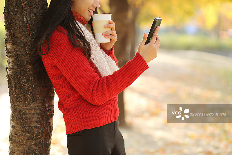 秋天，年轻女子用智能手机喝咖啡图片素材