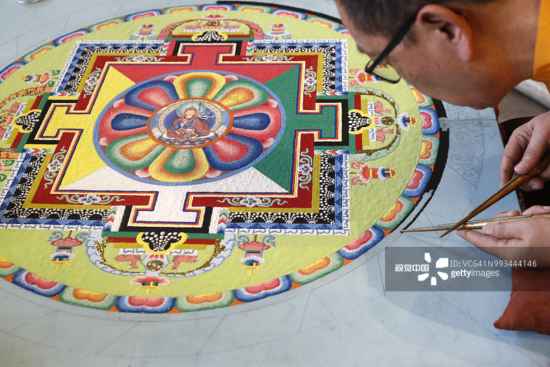 一位藏传僧人正在精心制作一个彩色的沙坛。图片素材