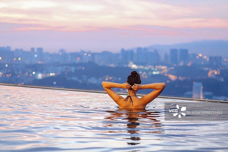 年轻女子放松在游泳池里，太阳在吉隆坡上空落下图片素材