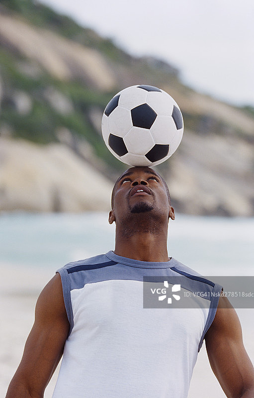 一个年轻人的特写，在他的头上平衡一个足球图片素材