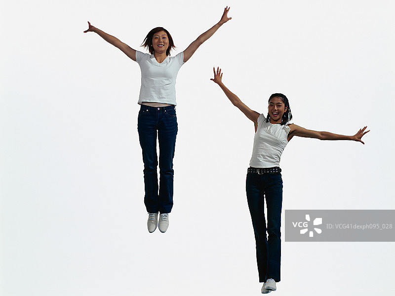 两个穿着牛仔裤和t恤的年轻亚洲女人，在半空中跳着图片素材