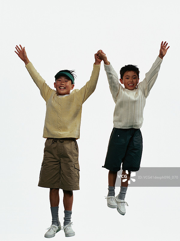 两个年轻的亚洲男孩穿着短裤和运动衫，跳在半空中图片素材