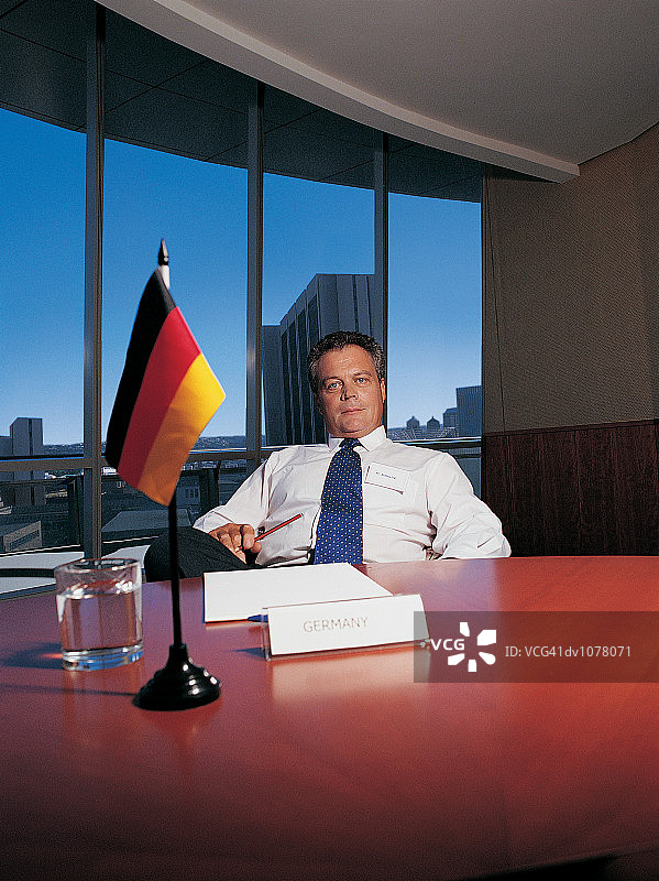 一个成熟的商人坐在德国国旗旁的会议桌旁的肖像图片素材