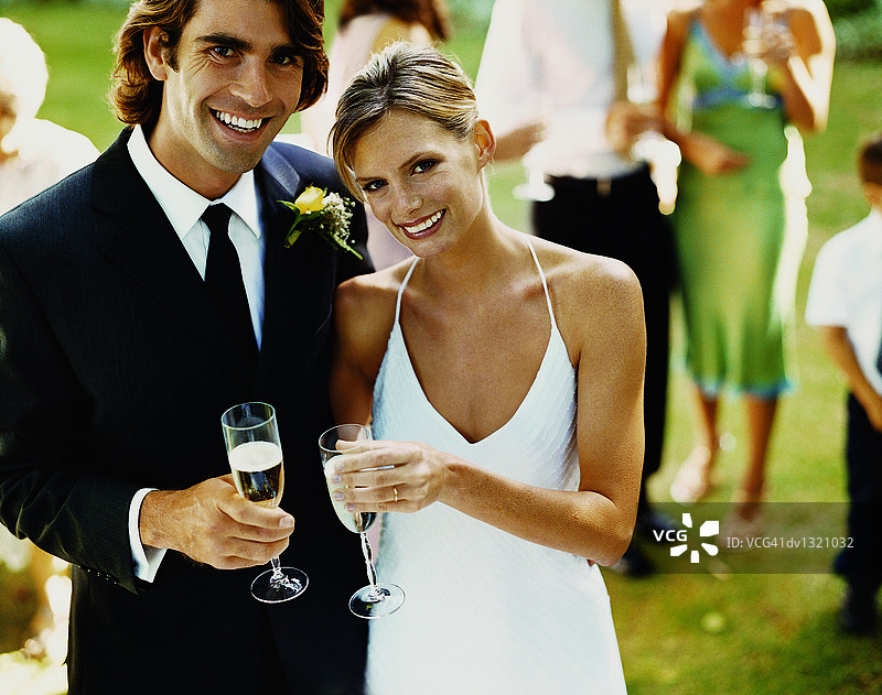 新婚的新娘和新郎与香槟杯站在草地上的肖像图片素材