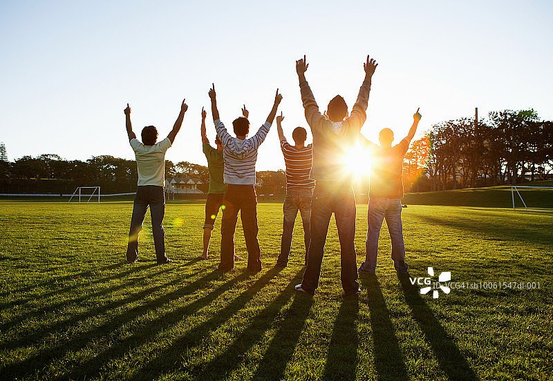 一群男人在公园里，向太阳伸出手臂，后视图图片素材
