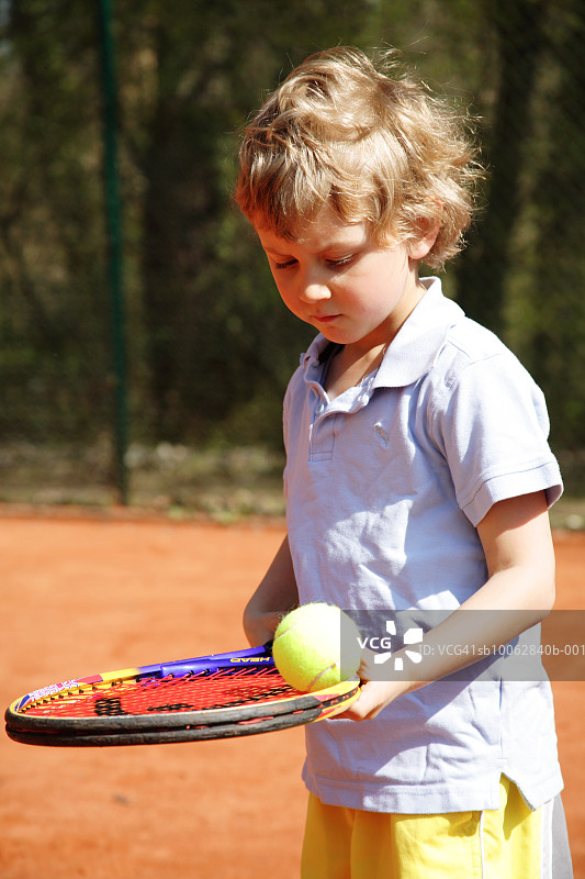 男孩(5-6岁)在室外场地的球拍上平衡网球图片素材