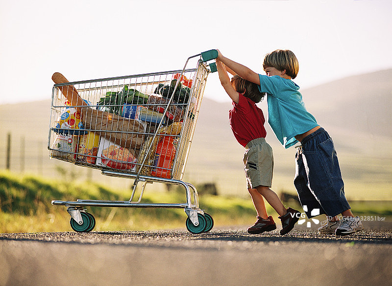 两个小孩推着一个装着杂货的购物车图片素材