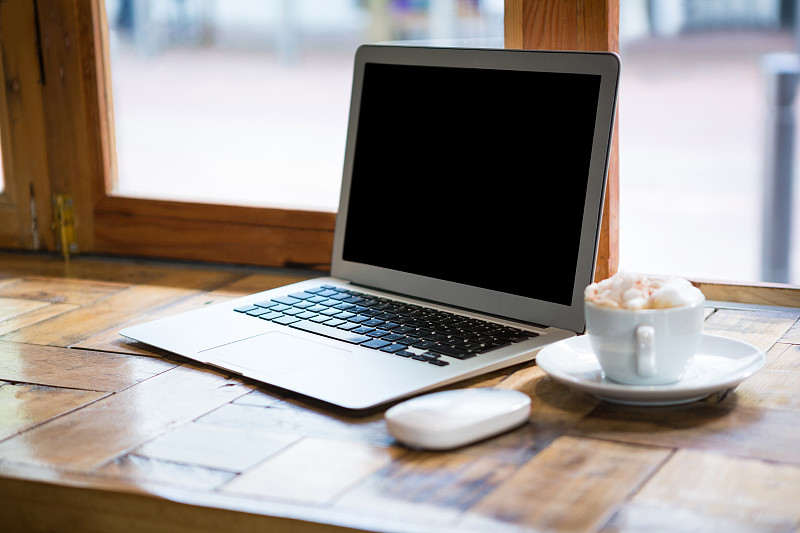 咖啡馆桌上咖啡杯旁的笔记本电脑特写图片素材