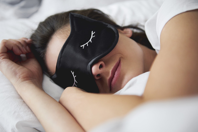 一张年轻女子戴着睡眠面罩躺在床上的肖像图片下载