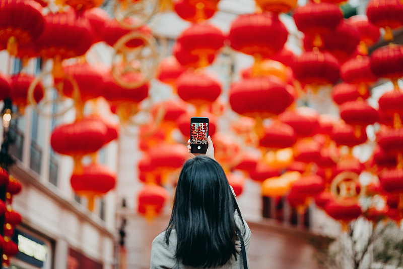 在城市街道上用智能手机拍摄传统中国红灯笼的女人的后视图图片下载