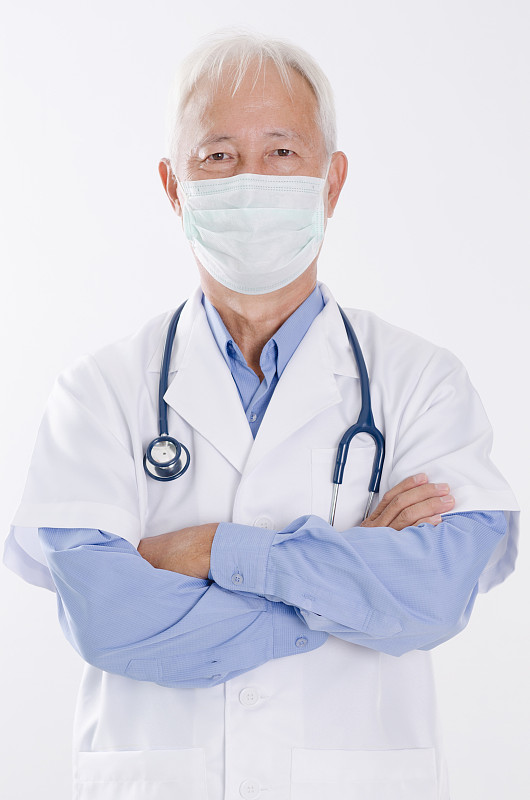 自信的资深医生穿着手术服站在白色的背景下图片素材