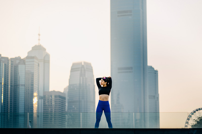 自信和决心的亚洲女运动员伸展双臂在户外对着城市景观日落图片素材