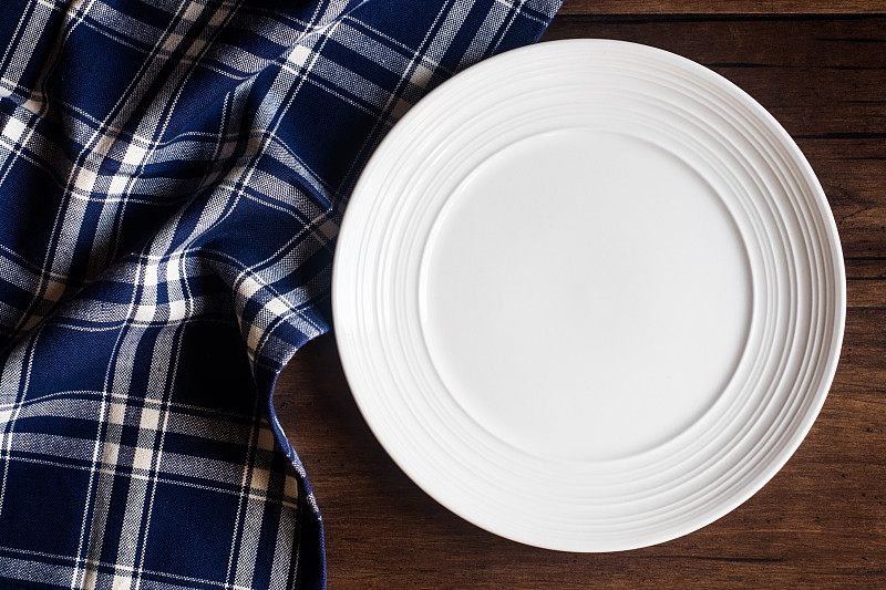 空的白色盘子和餐巾在一个旧的木制棕色背景，俯视图。图像与复制空间。厨房桌子与毛巾和一个盘顶视图与复印空间。图片下载