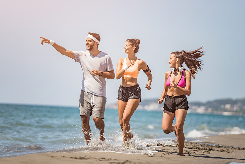 三个年轻的运动朋友一起在海滩上跑步。图片素材