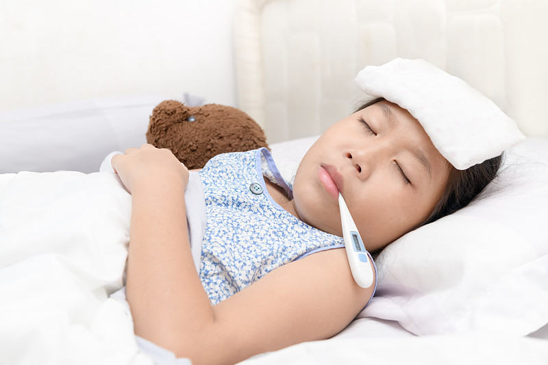 一个嘴含体温计的生病女孩躺在家里的床上图片素材
