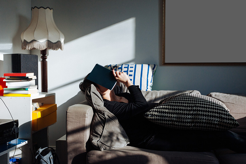 下午，一个年轻女子用一本书遮住脸睡在沙发上图片下载