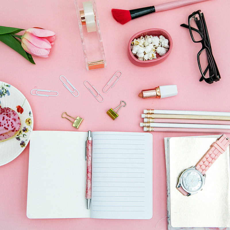 俯视图粉色笔记本，美容刷，郁金香和粉色唇膏，壁炉形状的甜甜圈在粉红色的背景图片下载