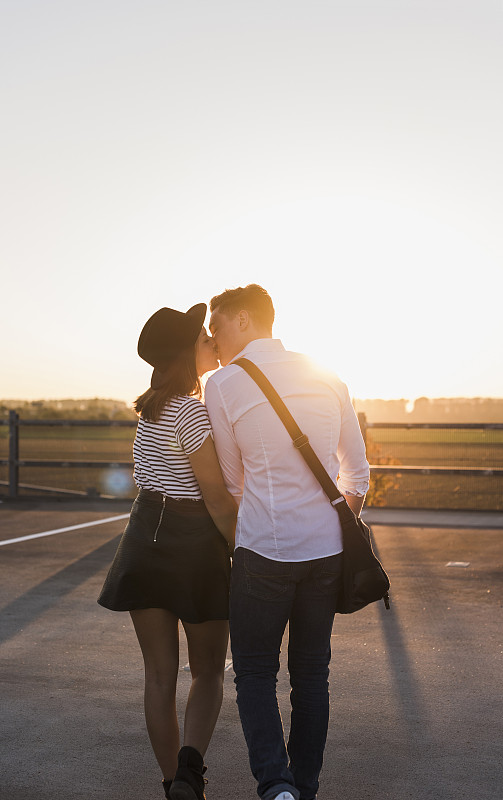 日落时分，一对年轻的情侣在停车场上接吻图片下载