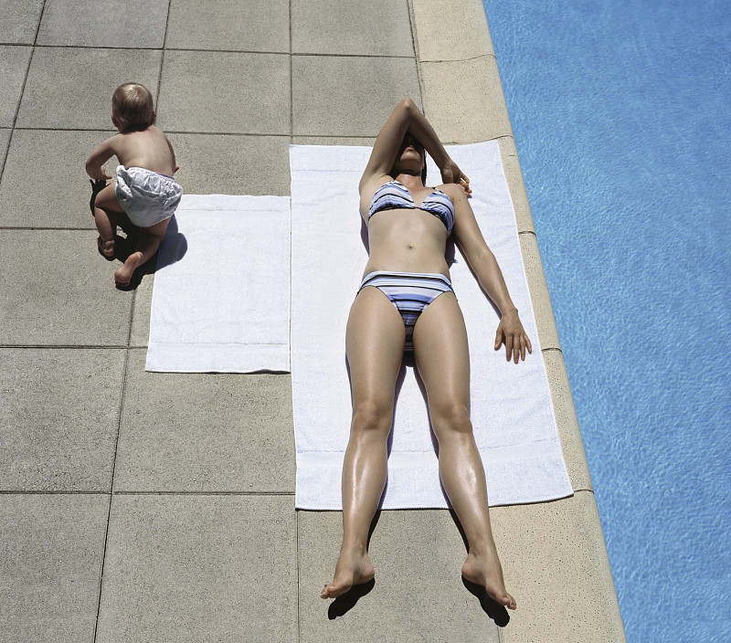 中年妇女在泳池边晒太阳，婴儿(5个月)爬走图片下载