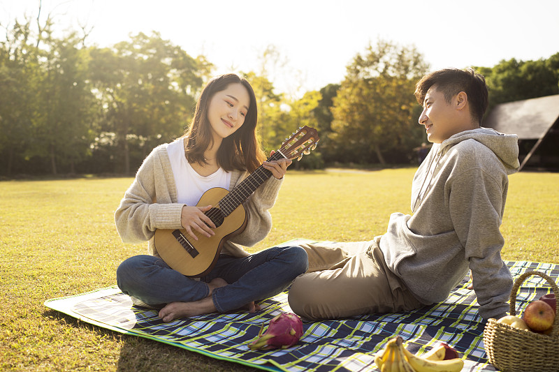 年轻情侣在草地上野餐演奏吉他图片下载