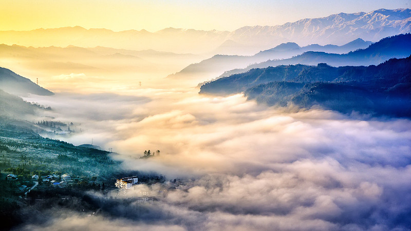 起伏绵延的山峦形成的山谷中被晨光照亮的流动云雾笼罩着山里人家图片下载