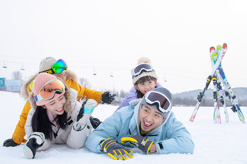 快乐的一家四口趴在雪地上玩耍嬉戏图片素材