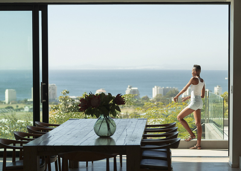 年轻女子站在现代化的阳台上，可以看到阳光明媚的海景图片下载