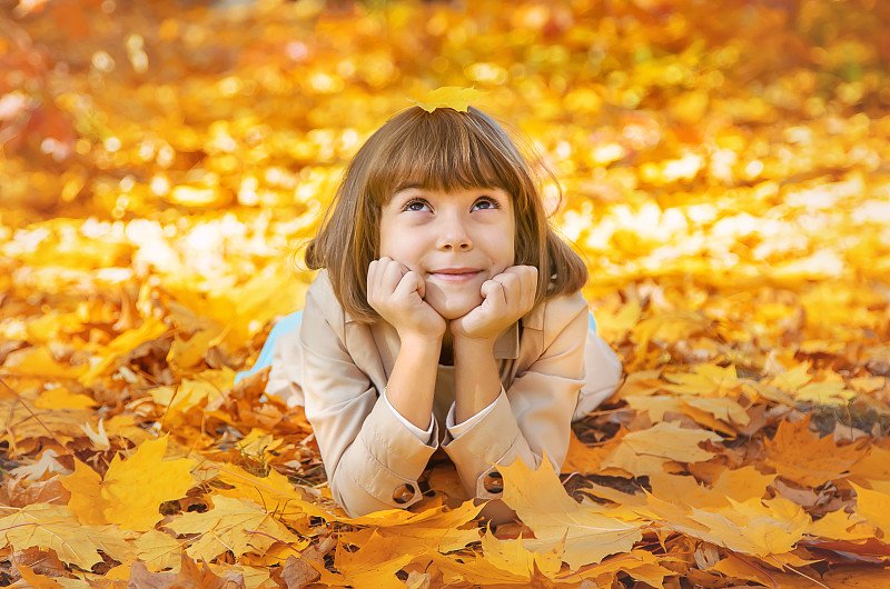 女孩趴在秋天的黄叶上图片素材