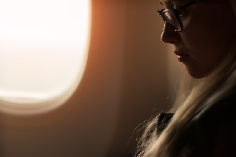 侧面的年轻女子与金发和眼镜坐在旁边的飞机窗口图片下载