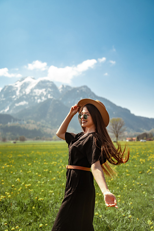 女孩穿着黑色的长裙，戴着棕色的帽子在山上的草地上图片素材