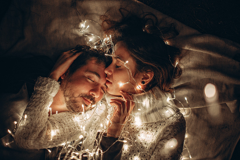巴西贝洛奥里藏特，一对夫妇躺在挂着圣诞彩灯的床上图片素材