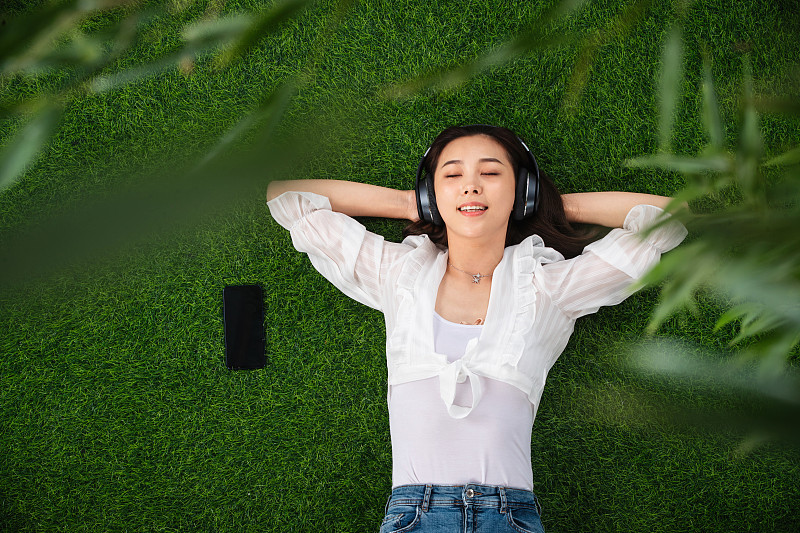 躺在草地上听音乐的青年女人图片下载