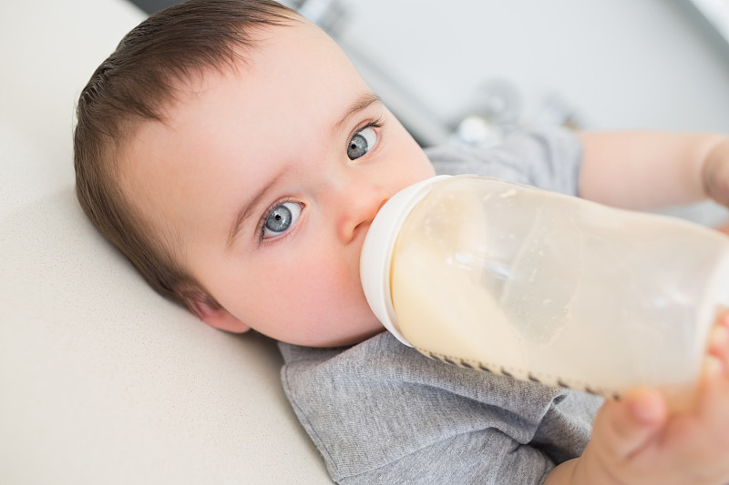 高角度的肖像，天真的婴儿喝牛奶，而躺在厨房柜台图片素材
