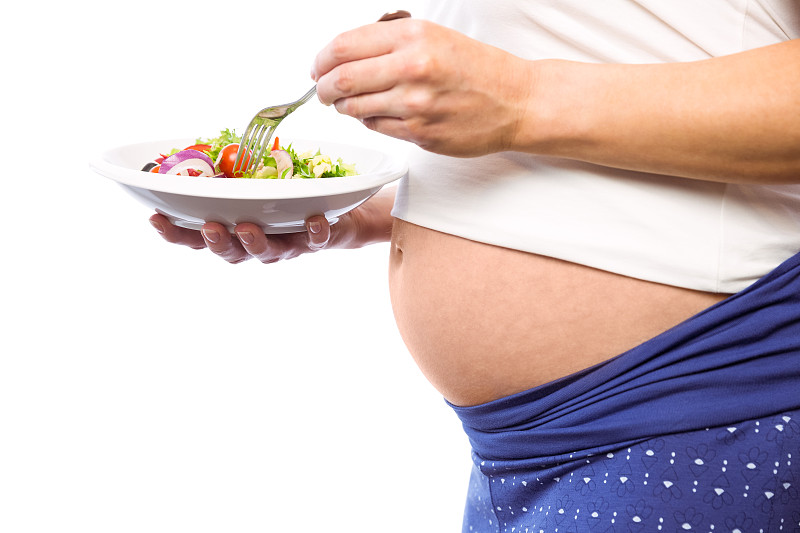 一名孕妇在白色背景下吃沙拉图片素材