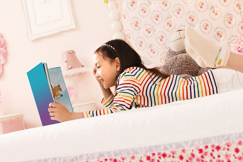 可爱的小女孩在卧室看书图片素材
