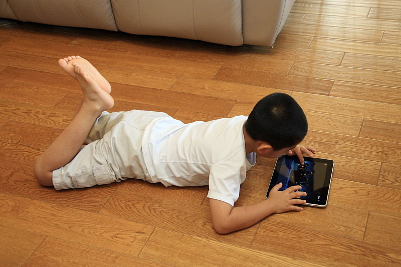 东方男孩趴在地板玩电脑图片素材