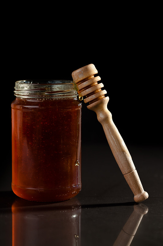 蜂蜜罐和蜂蜜勺在黑色背景下图片下载